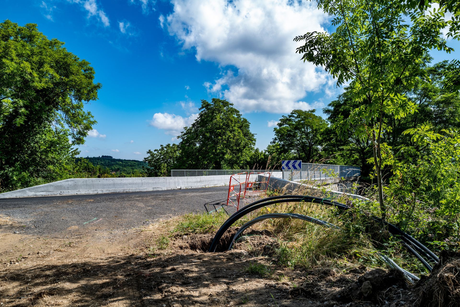 Travaux routiers sur un chemin de gravier sinueux bordé d'arbres sous un ciel d'un bleu éclatant.