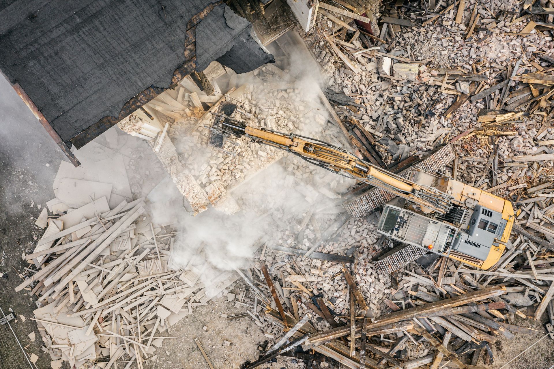 Une pelleteuse démolit un bâtiment, projetant des débris et de la poussière sur le chantier.