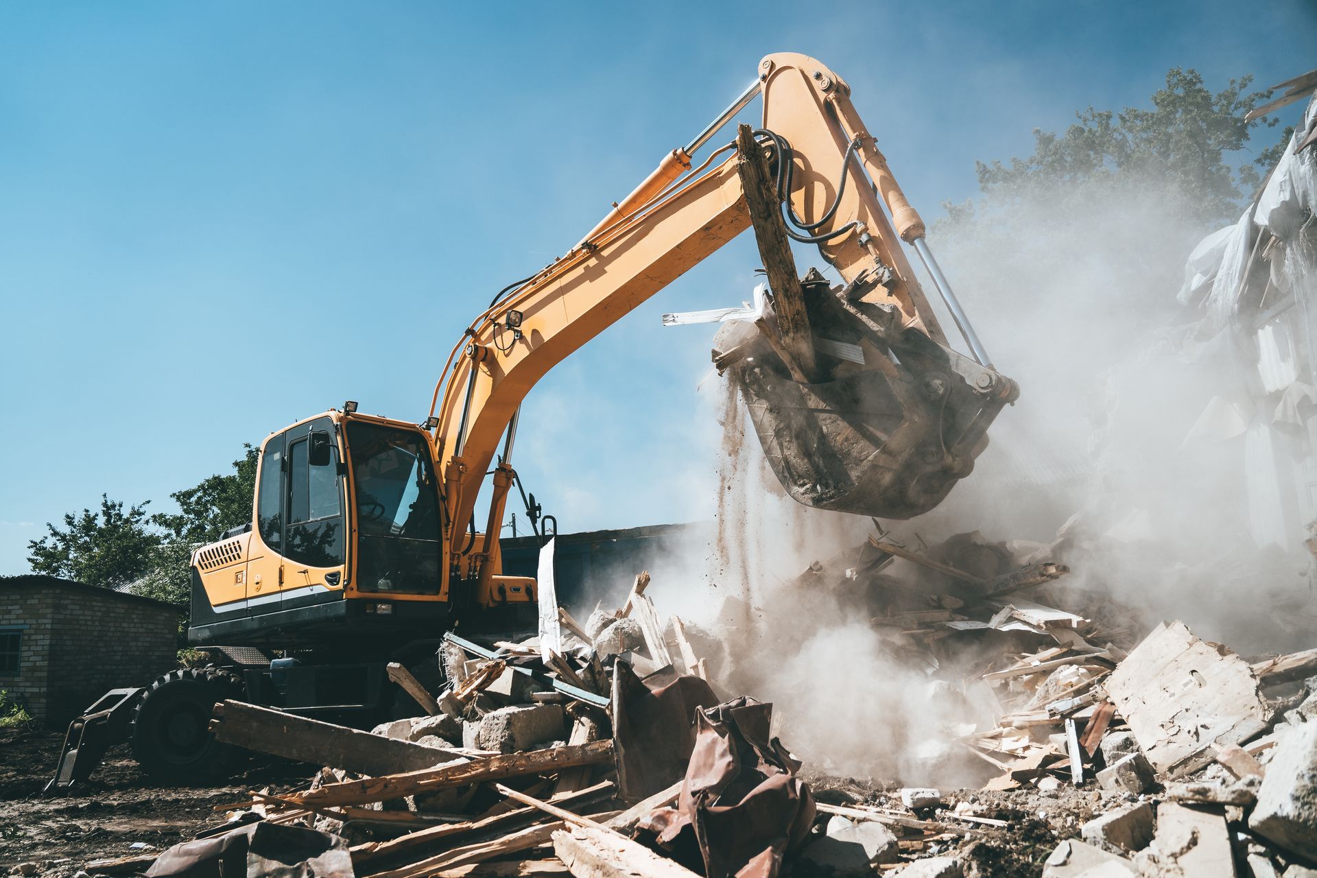 Une excavatrice démolit des gravats tandis que la poussière s'élève sur un chantier de démolition.