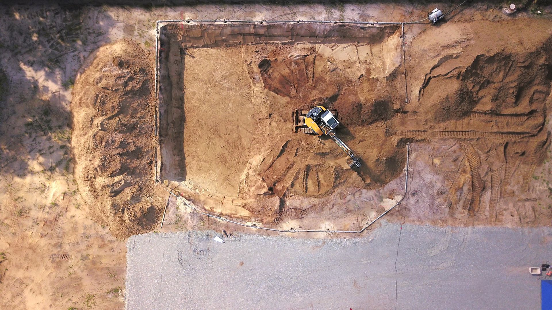 Vue aérienne d'une excavatrice jaune creusant à côté d'une fosse et d'une route.