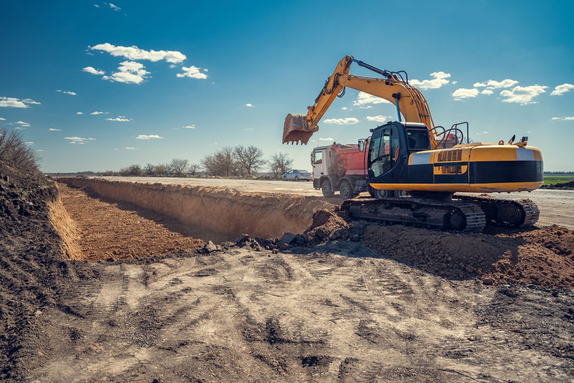 Une excavatrice charge de la terre sur un chantier de construction sous un ciel bleu.