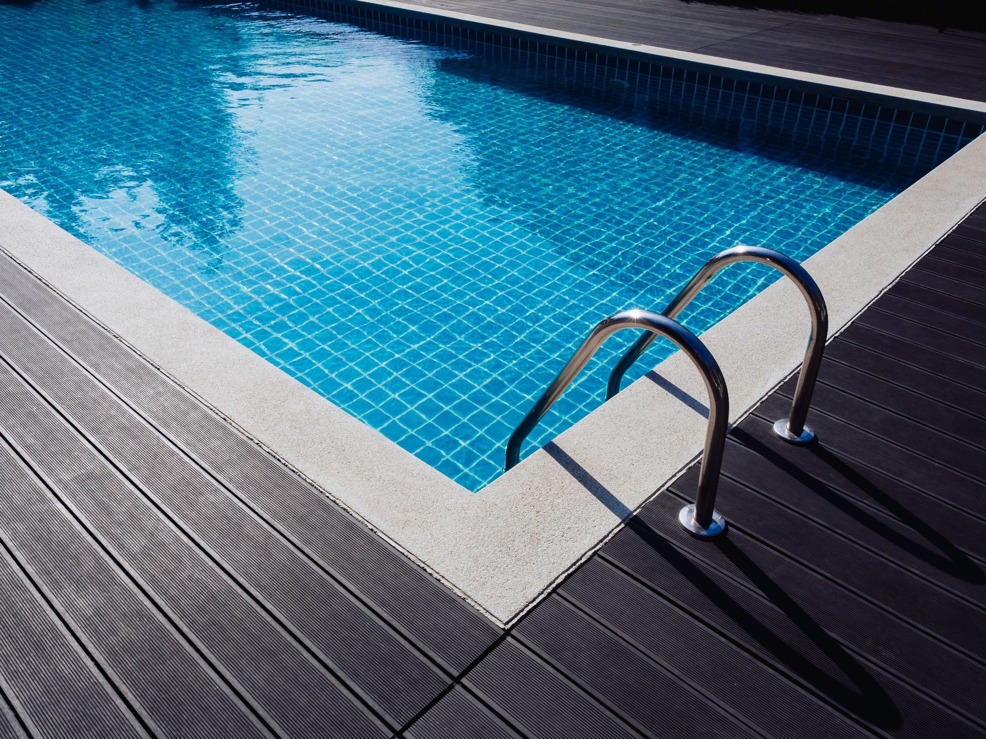 Coin piscine avec échelle métallique et eau bleue à côté d'une terrasse en bois.