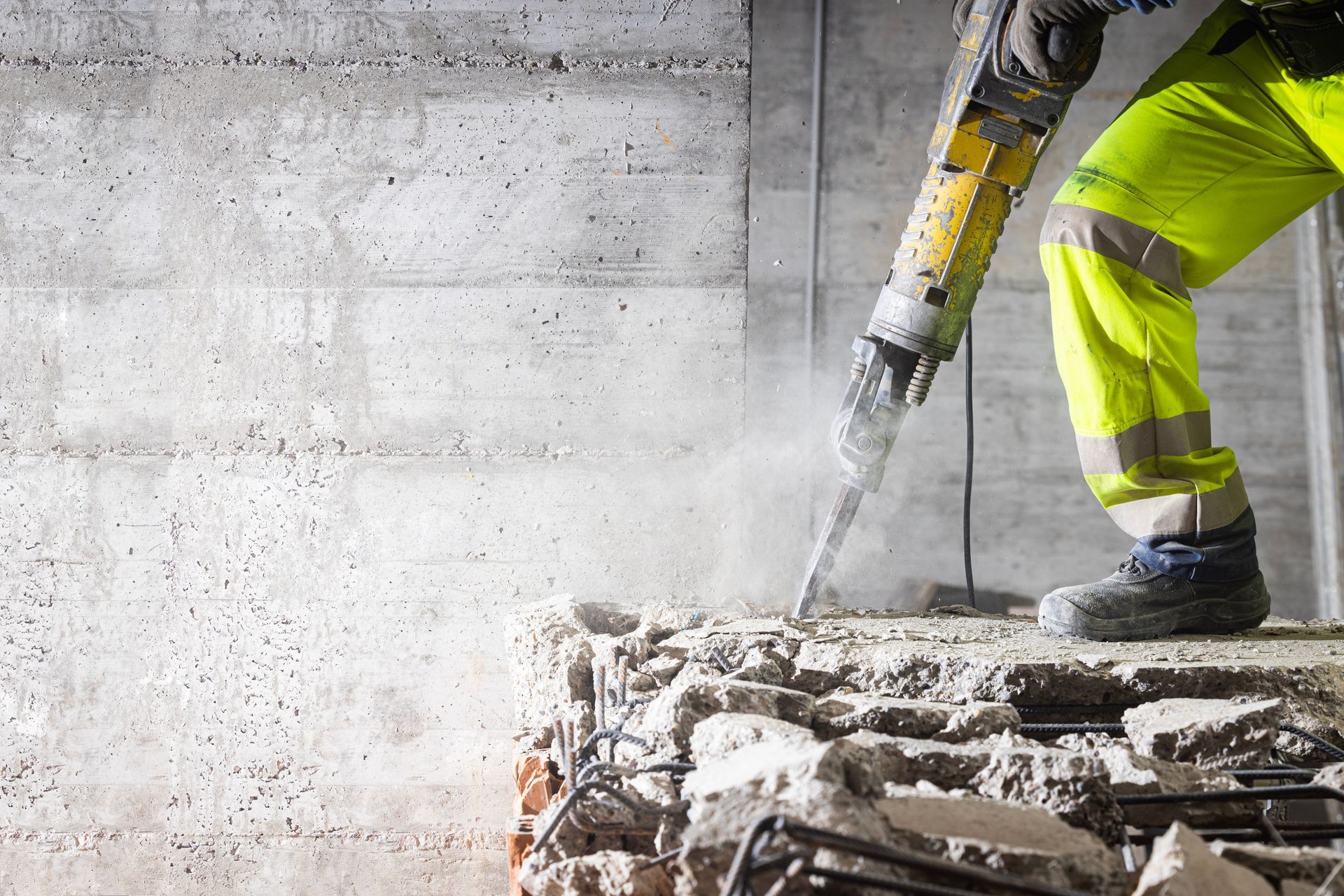 Un ouvrier utilise un marteau-piqueur pour casser du béton sur un chantier poussiéreux.