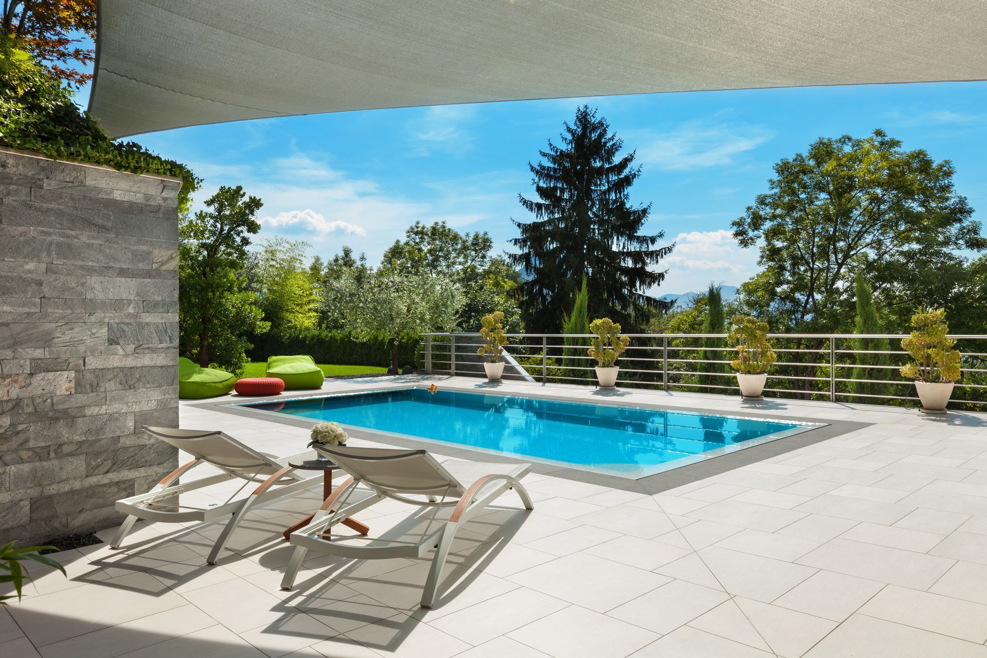 Terrasse moderne dans le jardin avec piscine, chaises longues et arbres au-delà de la clôture.