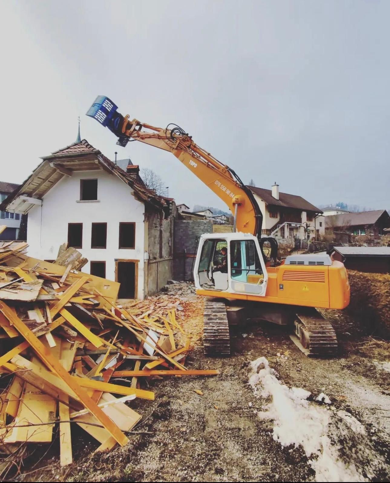 Machine de chantier à côté d'une maison en cours de destruction.