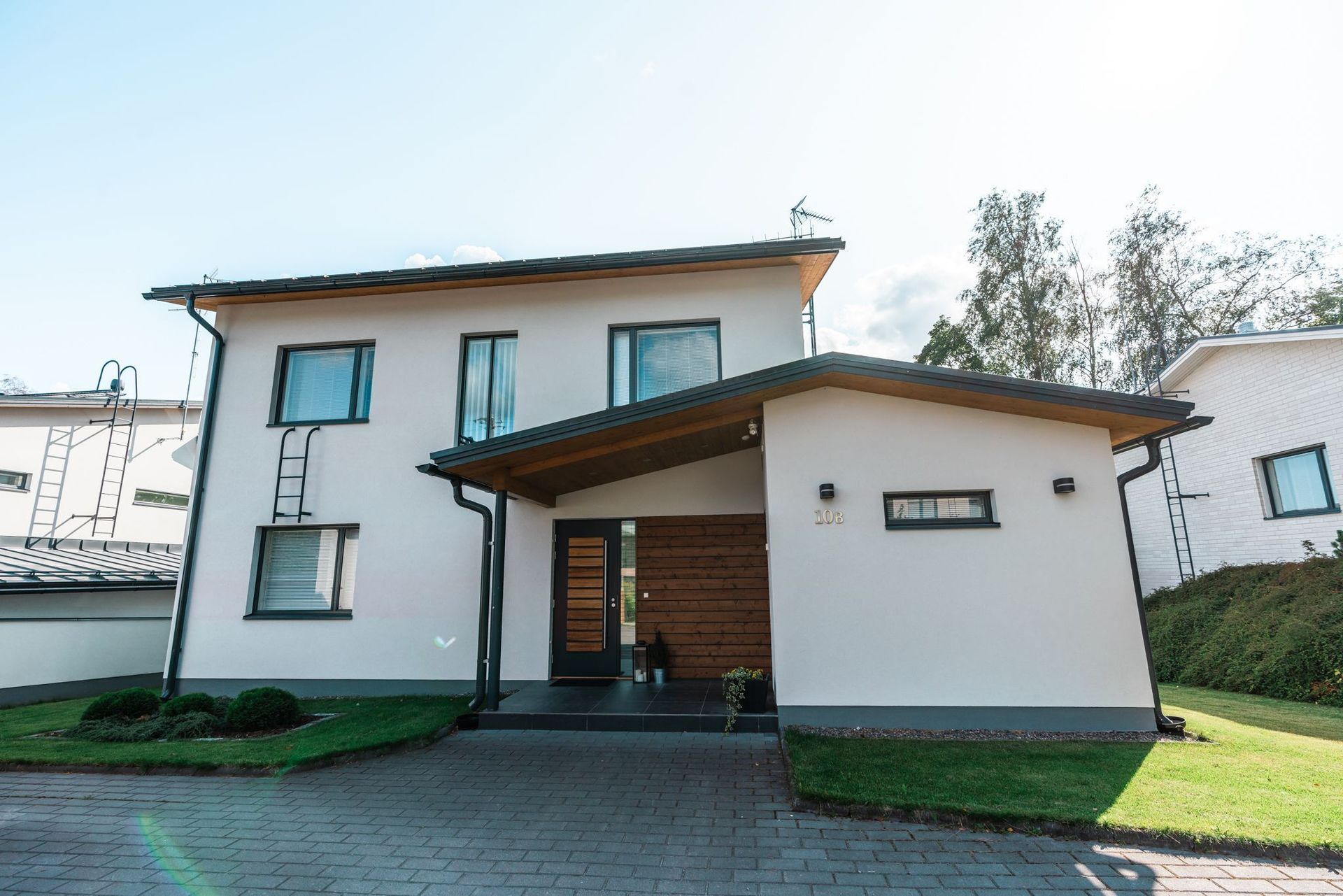 Moderni kaksikerroksinen valkoinen talo, jossa on ruskea katto ja autokatos