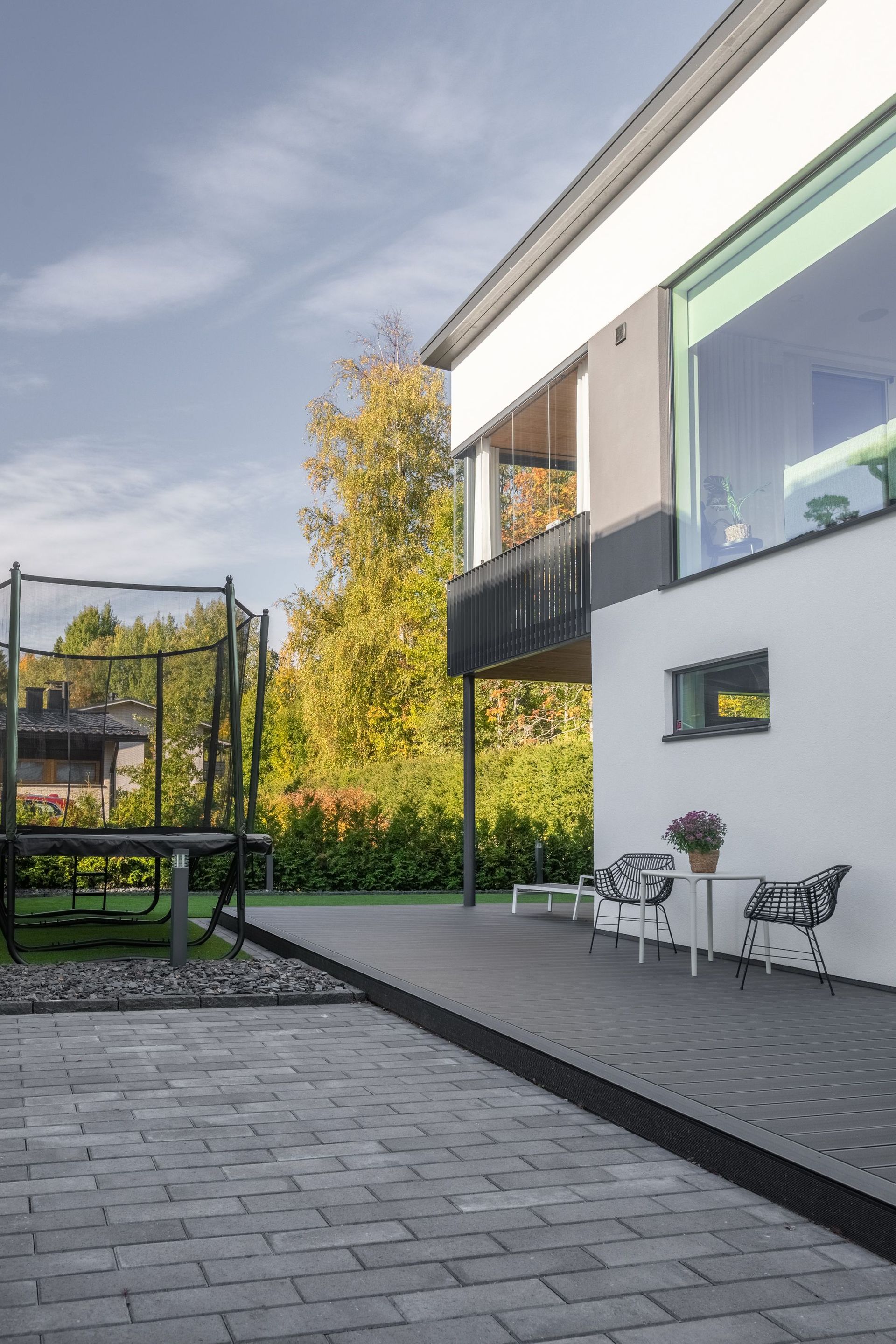Moderni talon patio, jossa on harmaita laattoja, ulkoistuimia ja pieni pöytä suurten ikkunoiden vieressä