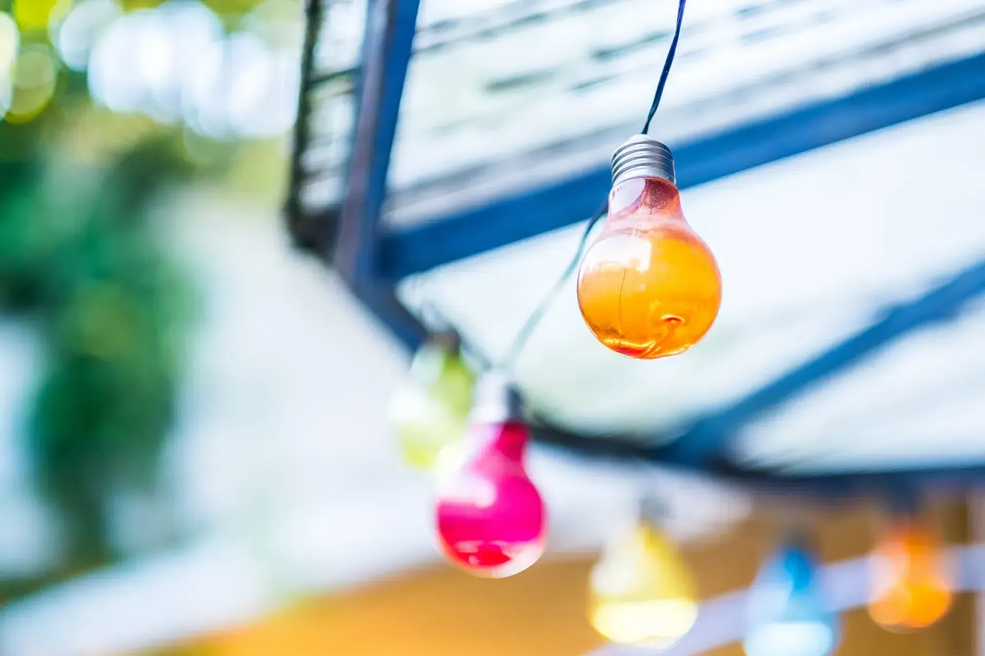 Une guirlande lumineuse colorée suspendue sous un toit transparent par une journée ensoleillée.