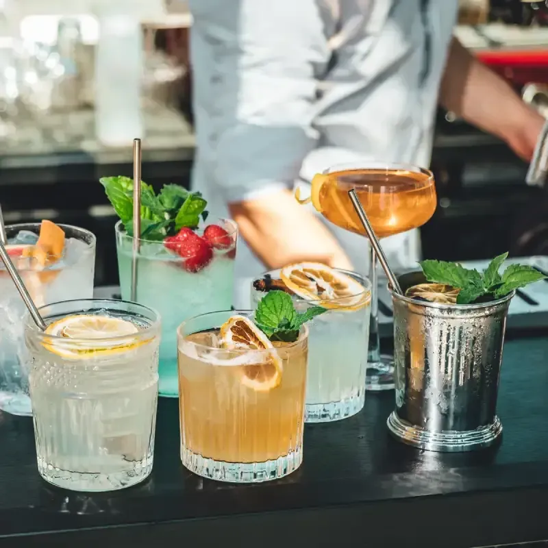 Un barman prépare des cocktails derrière un comptoir, mettant en valeur une variété de boissons colorées et décorées.