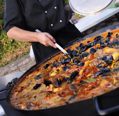 Une personne tient un ustensile dans un récipient contenant une paëlla