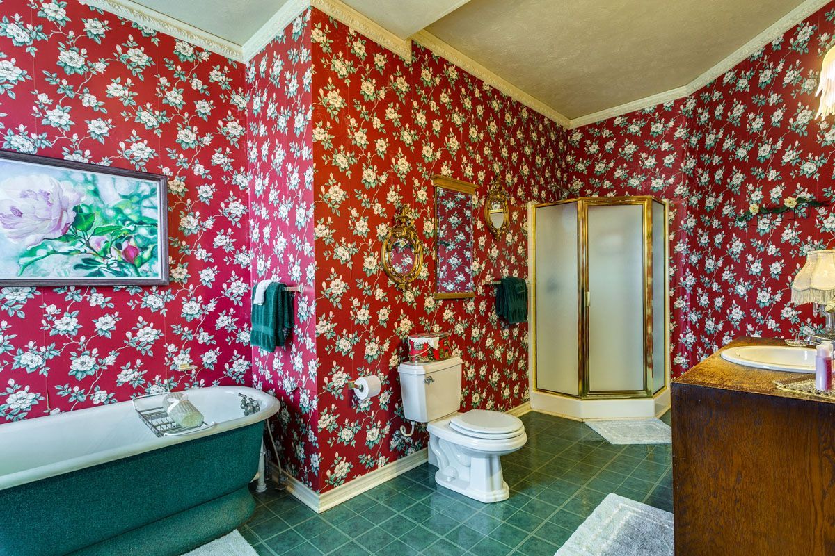 A bathroom with red floral wallpaper , a green tub , a toilet , and a shower.