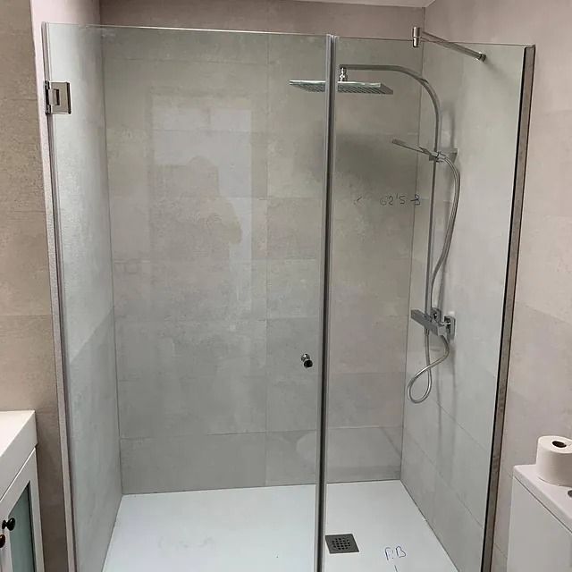 Un baño con ducha a ras de suelo con puerta de cristal y cabezal de ducha.