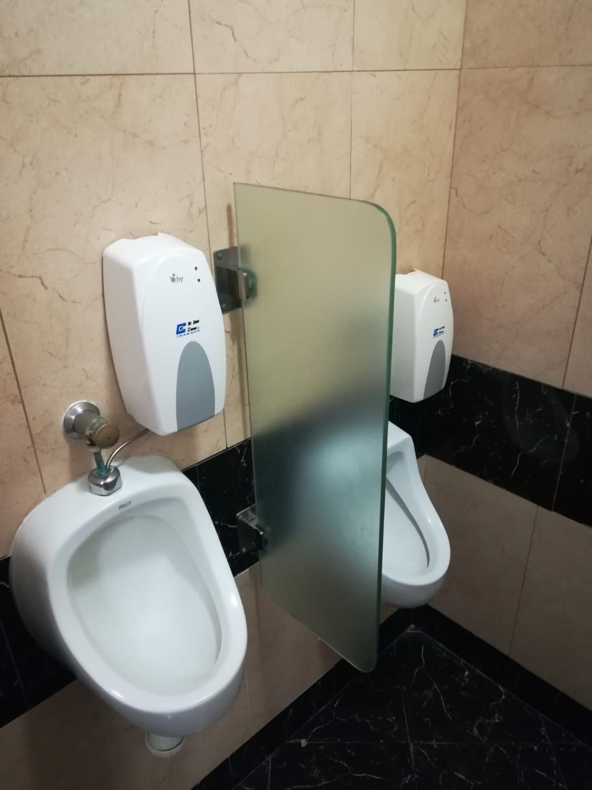 Un baño con dos urinarios y un dispensador de jabón.