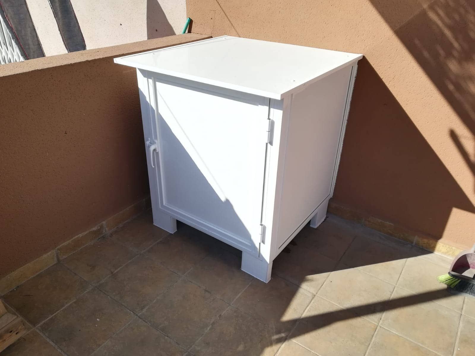 Un armario blanco está colocado sobre un suelo de baldosas en un balcón.