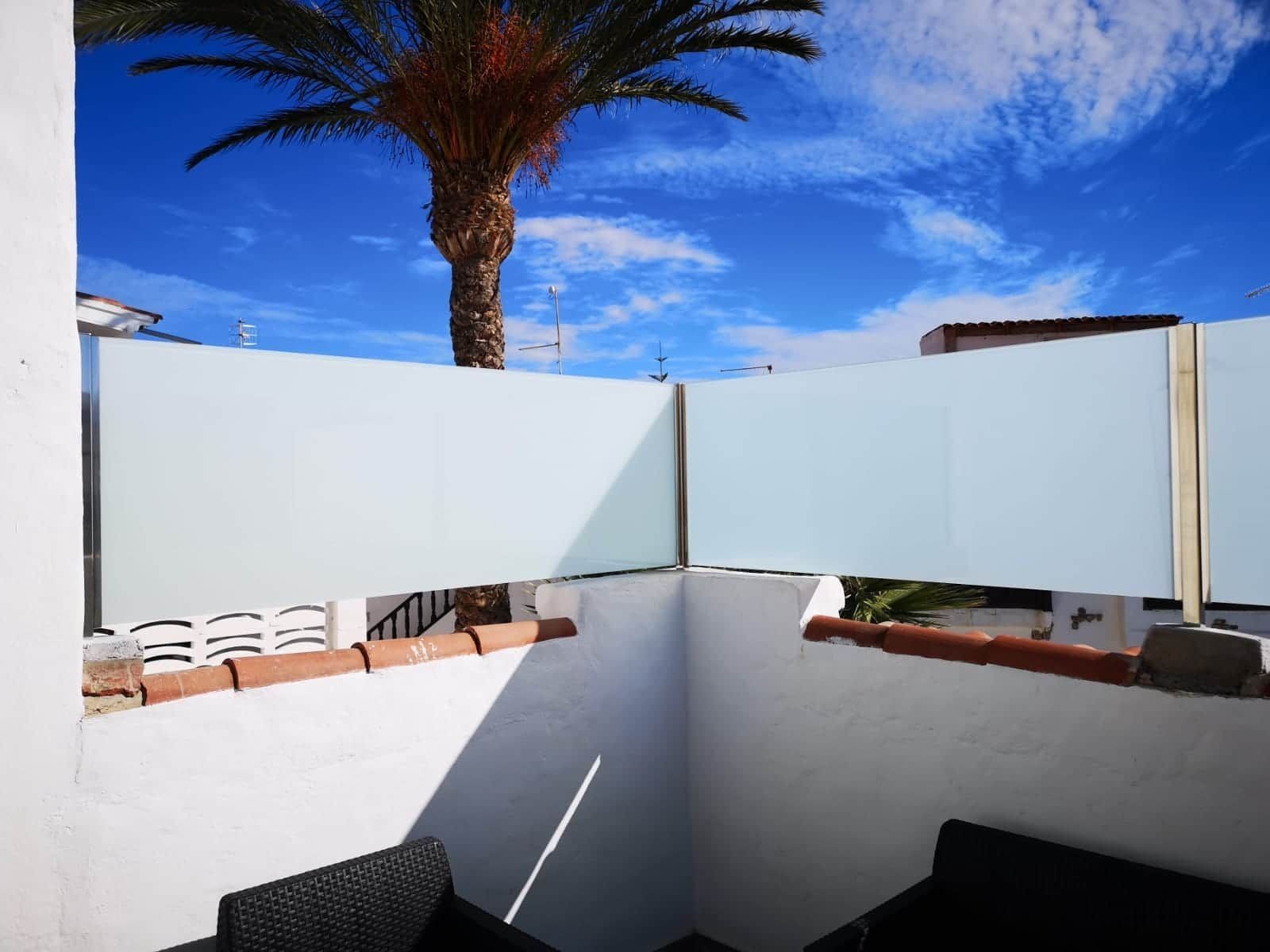 Un balcón con una valla de cristal y una palmera al fondo.