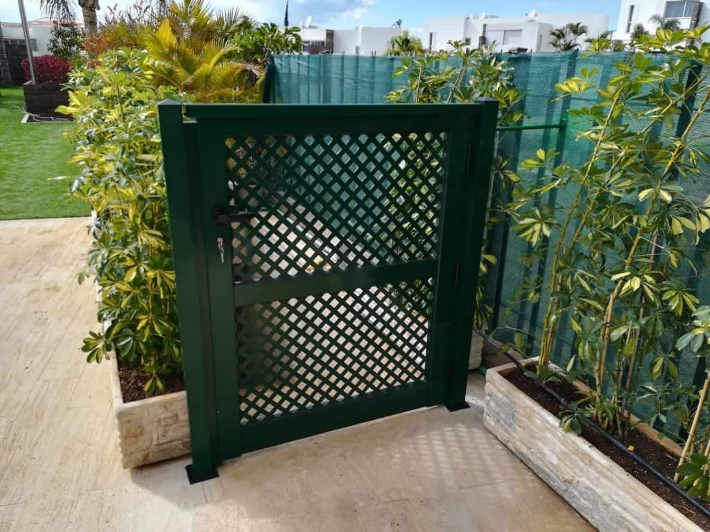 Una valla de celosía verde está rodeada de plantas en macetas.