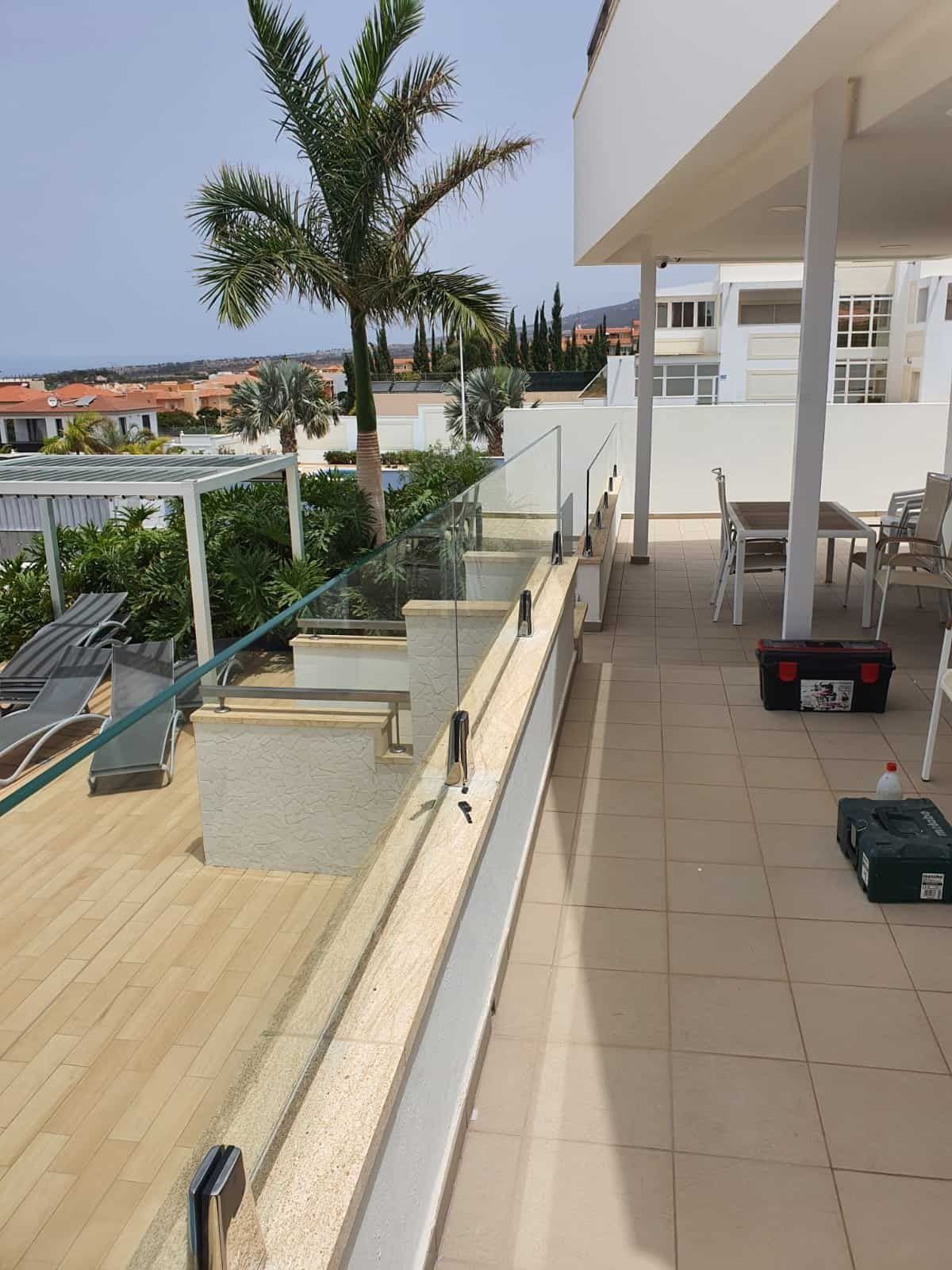 Un balcón con barandilla de cristal y una caja de herramientas en el suelo.