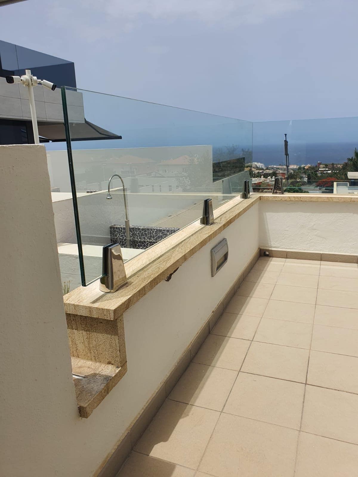 Un balcón con barandilla de cristal y vista al mar.