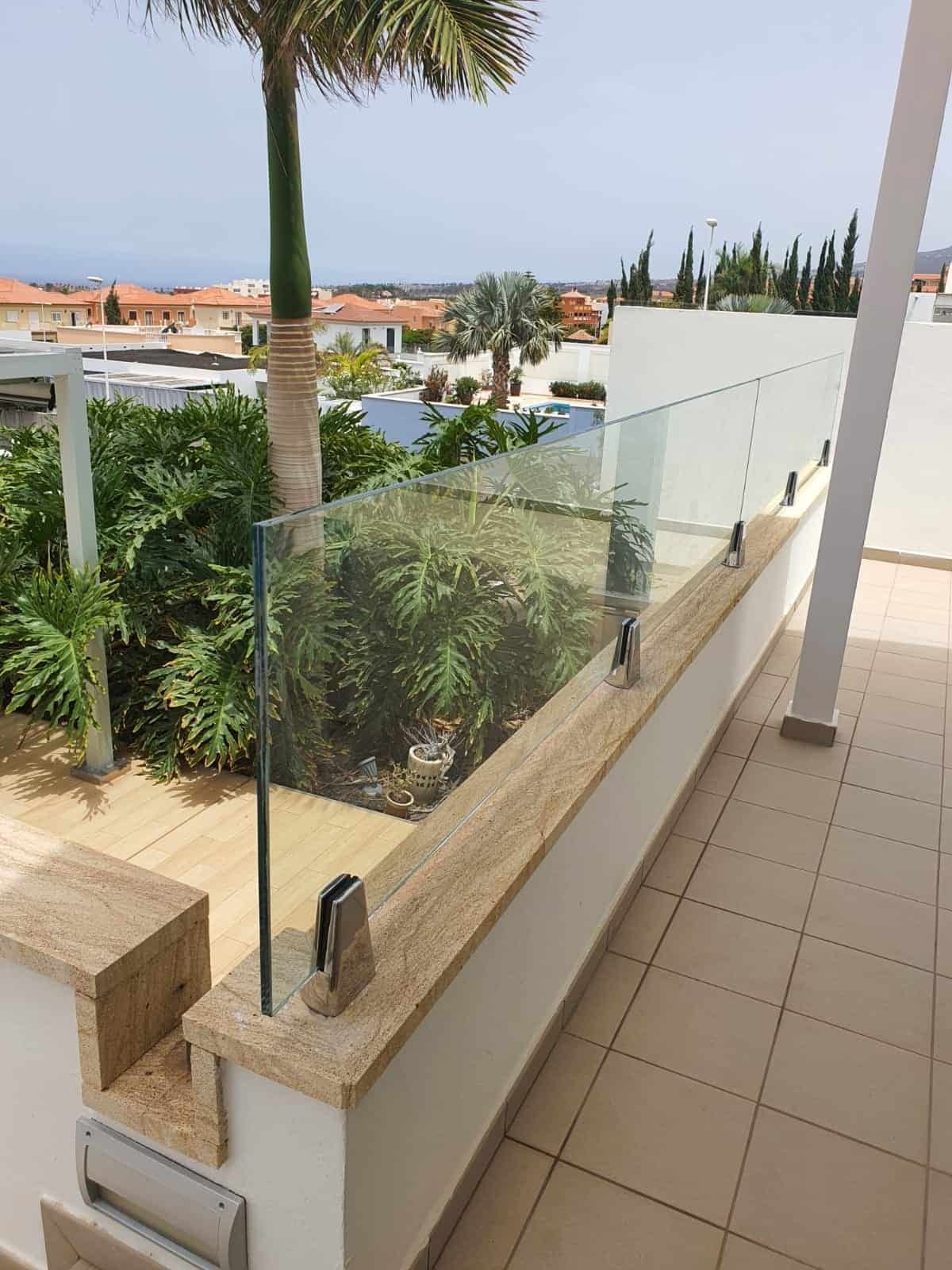 Un balcón con barandilla de cristal y una palmera al fondo.