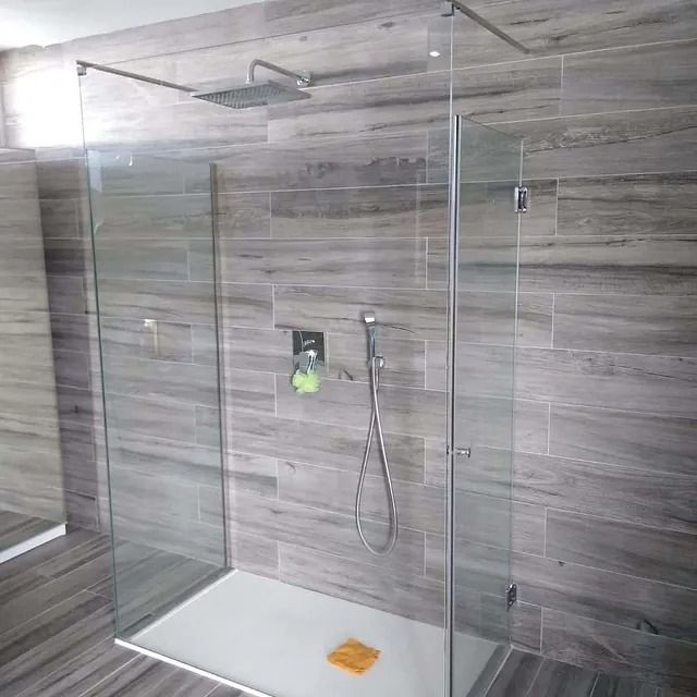 Una ducha a ras de suelo con puerta de cristal y cabezal de ducha.