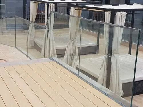 Un balcón con barandilla de cristal y suelo de madera.