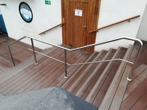 Una terraza de madera con escaleras y barandilla de acero inoxidable.