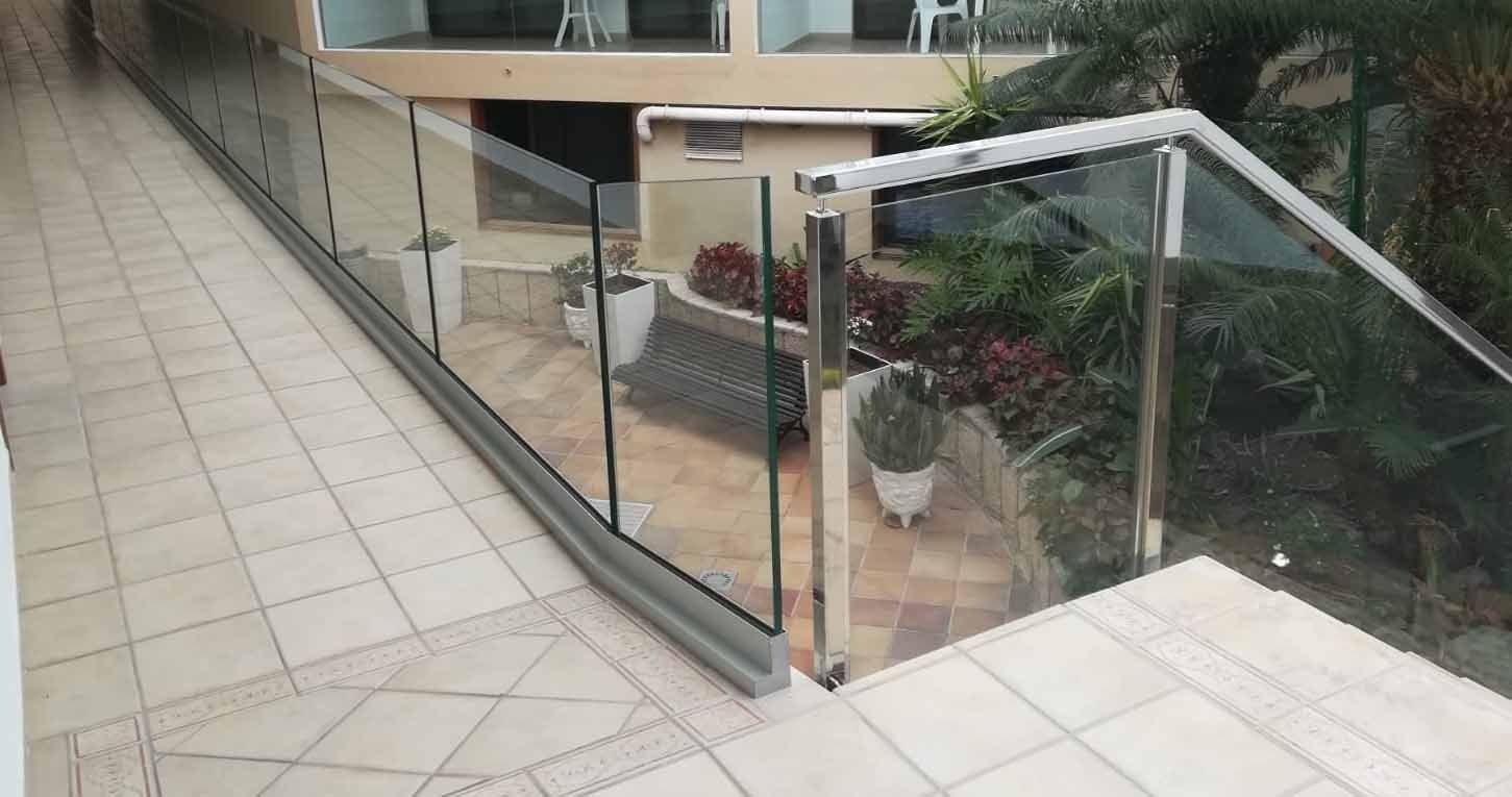 Un balcón con barandilla de cristal y escaleras que conducen al mismo.