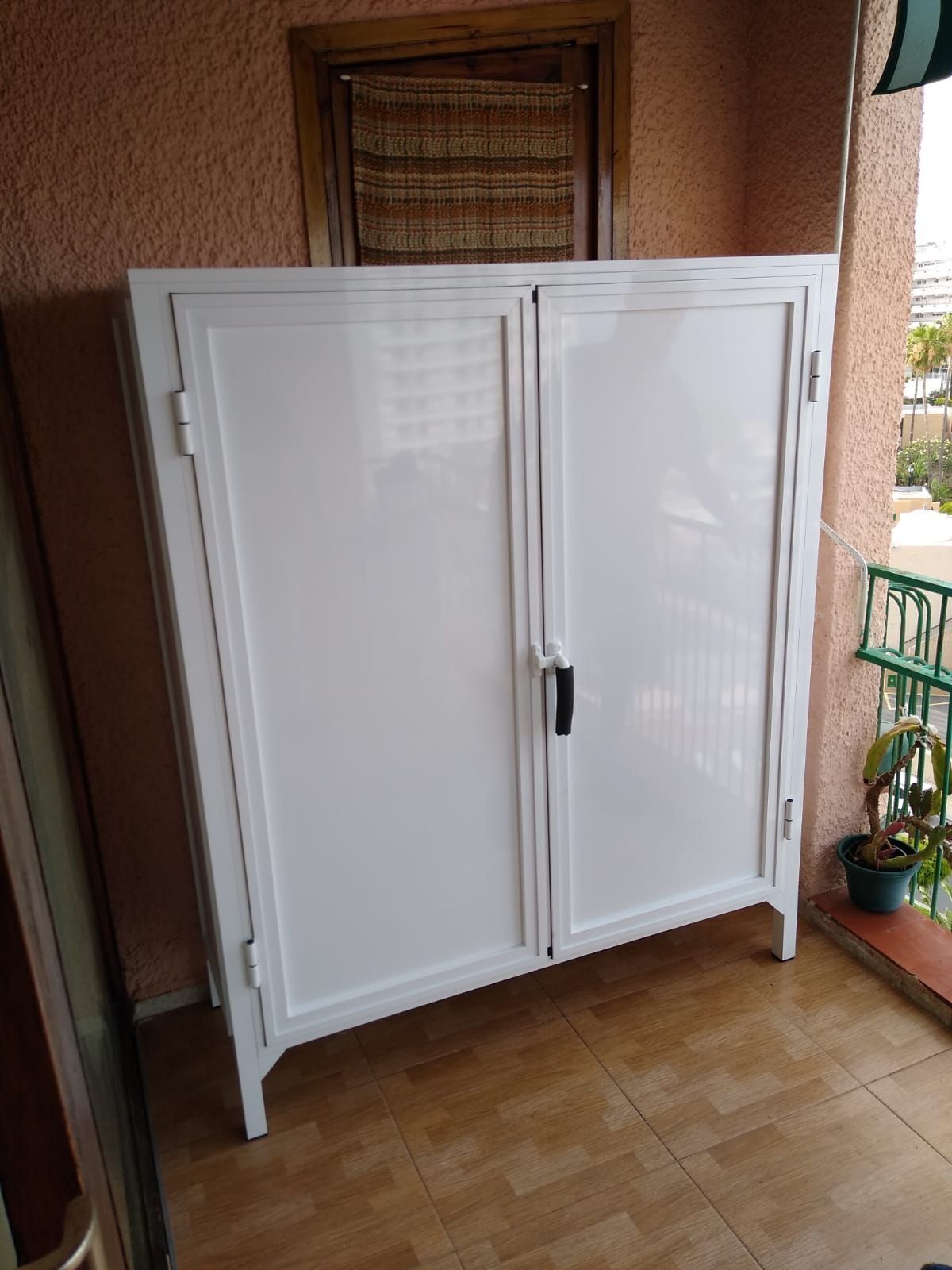 Un armario blanco está colocado sobre un suelo de baldosas en un balcón.