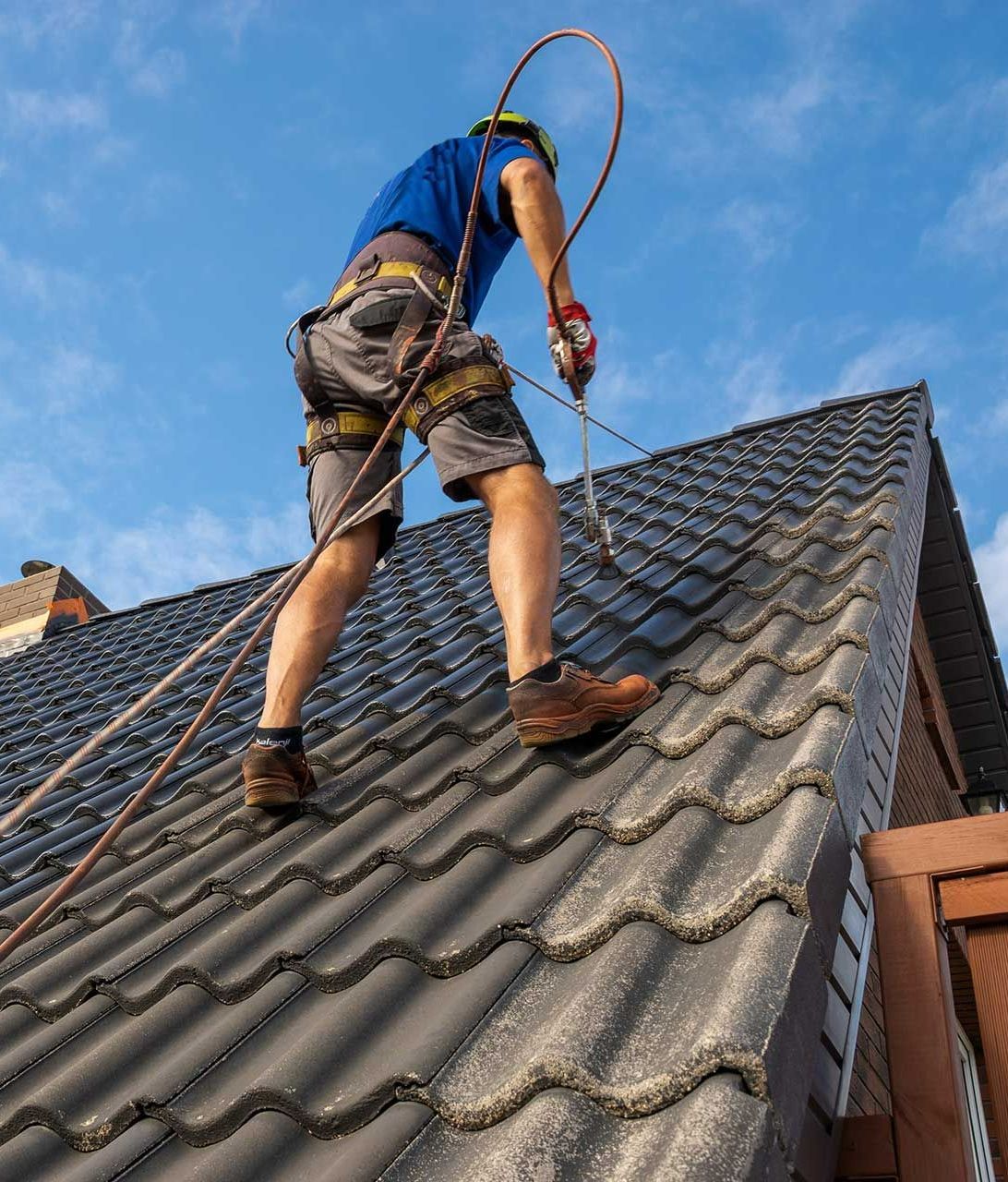 Homme qui applique du produit hydrofuge sur un toit à la couverture grise