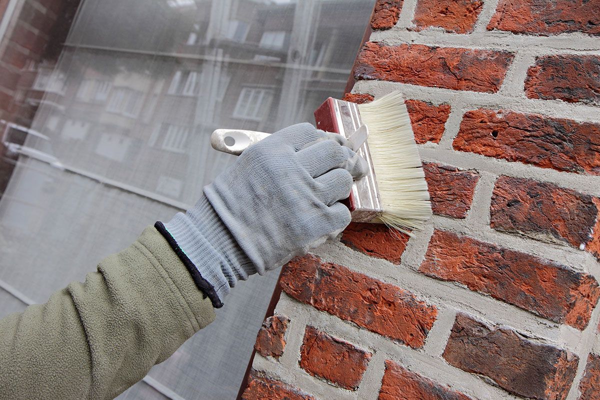 Homme applique de l'hydrofuge sur un mur en briques avec une brosse