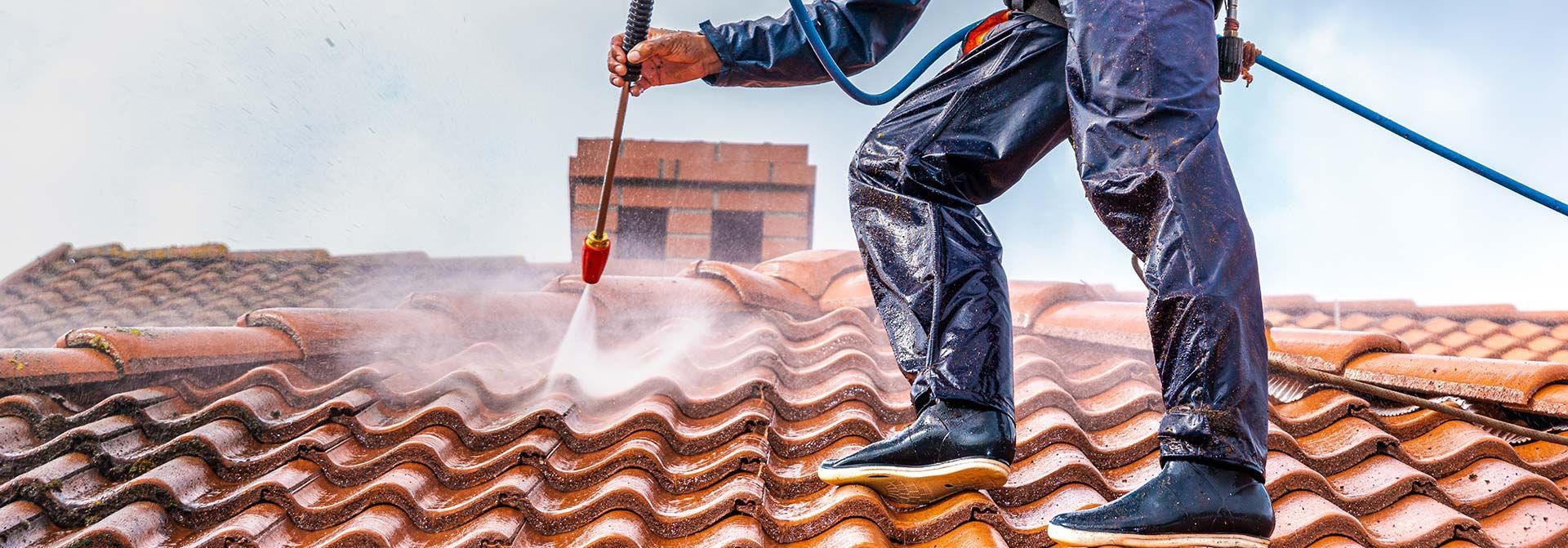 Homme sur un toit en train de passer le nettoyeur à haute pression