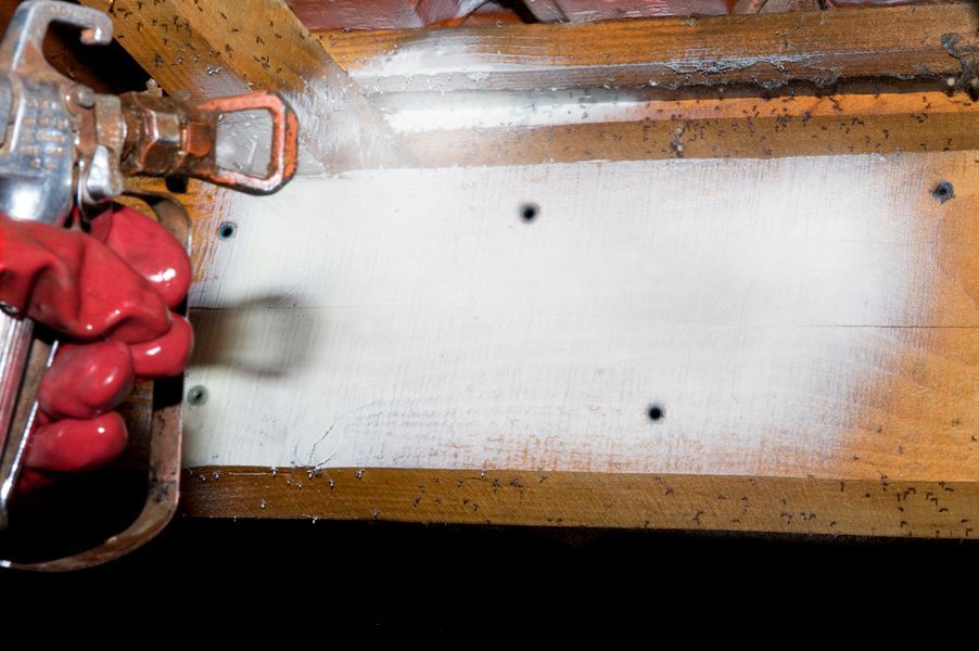 La main d'un homme applique du produit sur une poutre en bois par pulvérisation