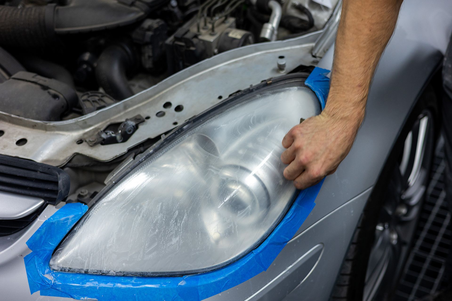 Eine Person reinigt einen Autoscheinwerfer mit blauem Klebeband.