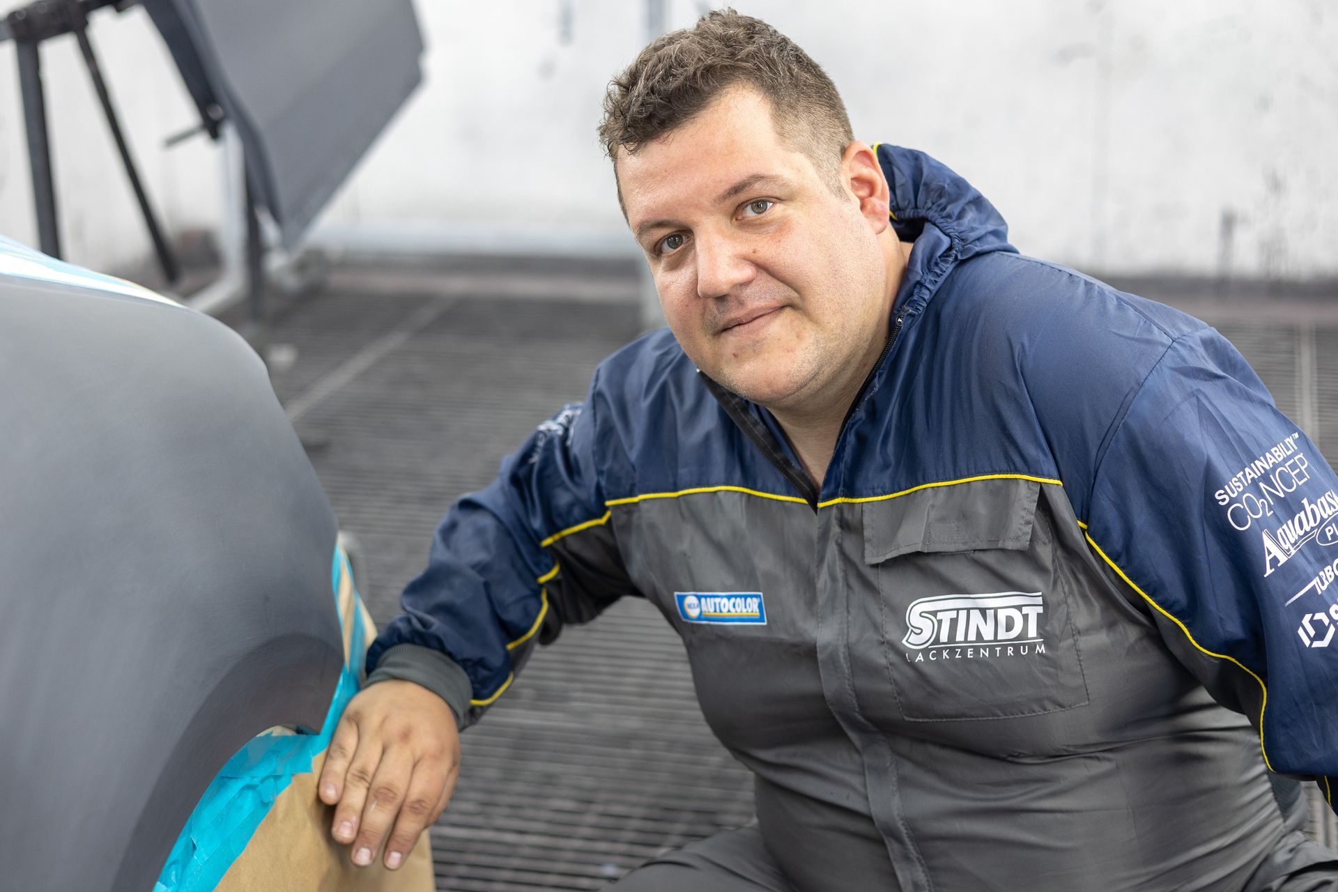 Ein Mann in einer blauen Jacke kniet neben einem Auto.