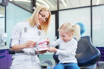 Un dentista le muestra a una niña cómo limpiarse los dientes.