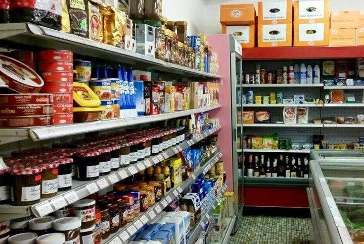 Une allée étroite d'épicerie avec des étagères remplies d'aliments emballés et une vitrine réfrigérée.