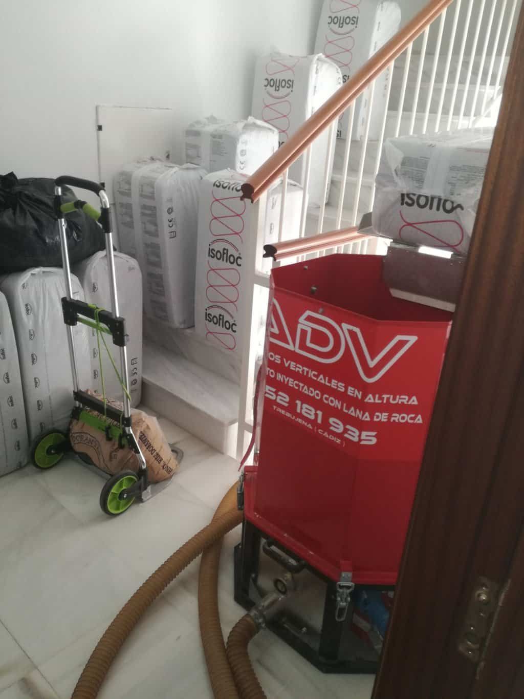 Máquina ADV roja, materiales aislantes y un carrito cerca de una escalera en una habitación.