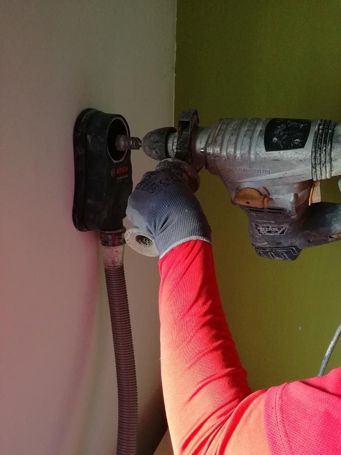 Persona que taladra un agujero en una pared con un taladro eléctrico, con una manga roja y un guante gris.