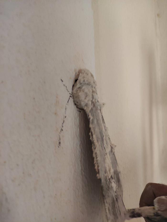 Pared blanca con un objeto colgante polvoriento y una pequeña grieta o marca oscura cerca.