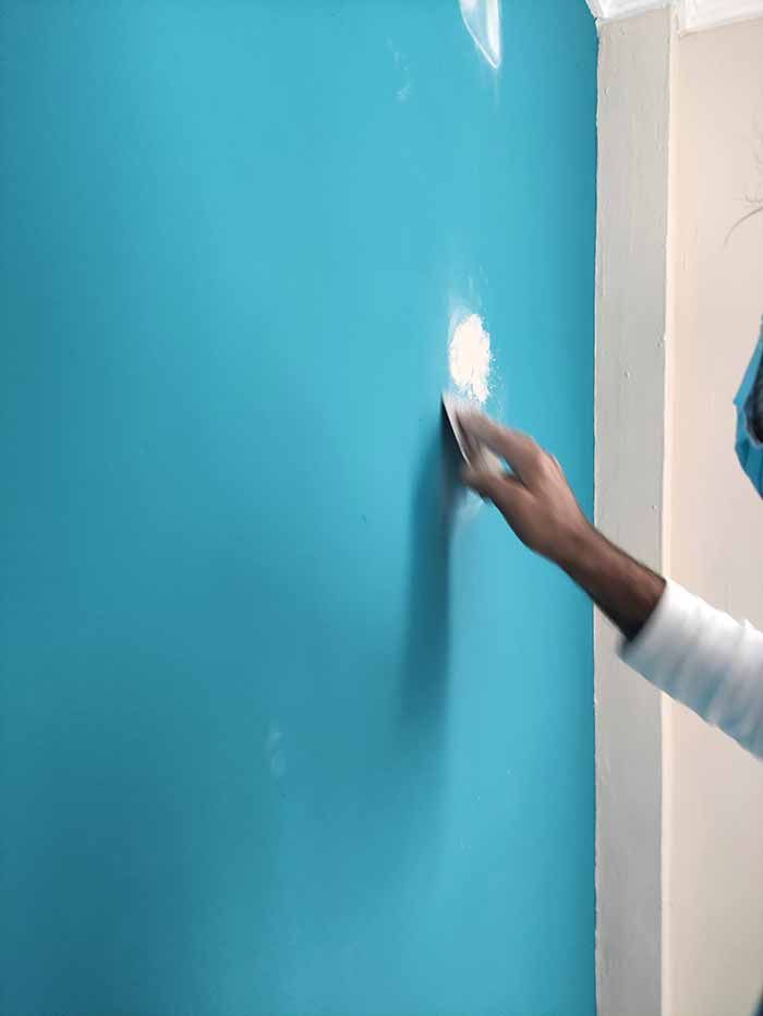 Alisando a mano pintura azul brillante en una pared cerca de una puerta.