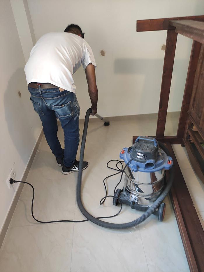 Un trabajador aspira un suelo de baldosas con una aspiradora industrial en una habitación en obras.