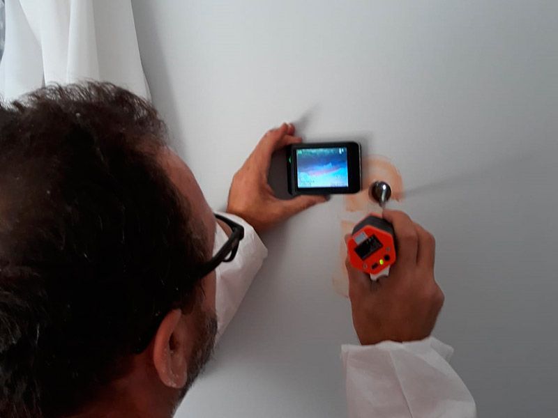 Un hombre inspecciona una pared con una cámara y una herramienta de medición