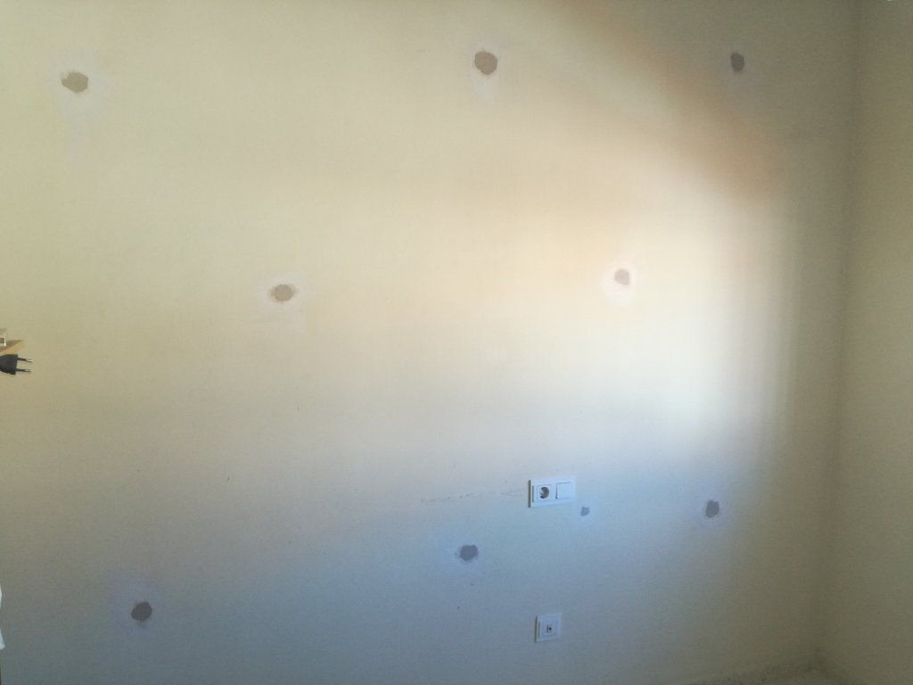 Pared beige con numerosos agujeros tapados, lo que sugiere reparaciones o preparación para pintar.