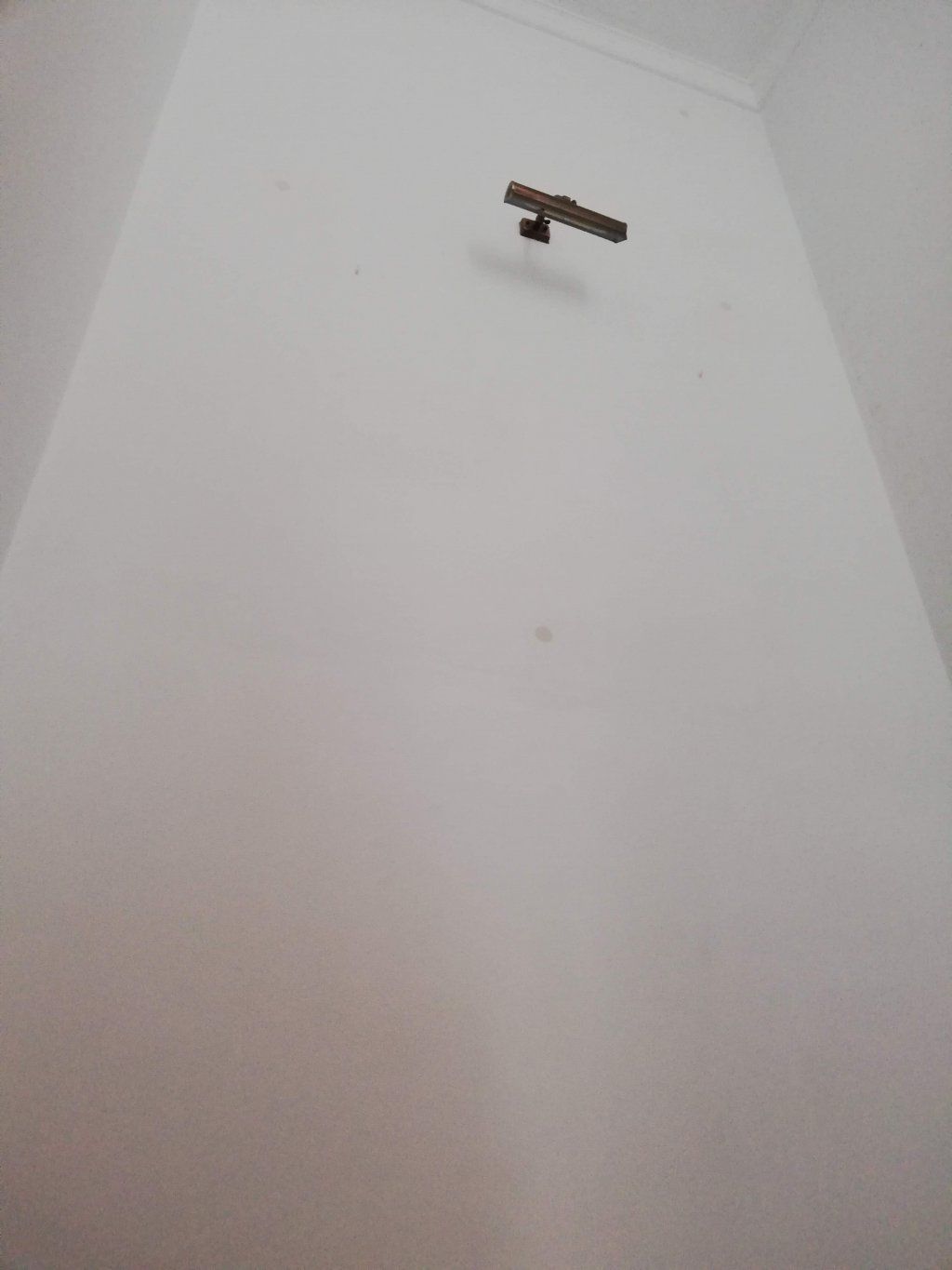 Pared blanca con una lámpara marrón en forma de T cerca de la parte superior.