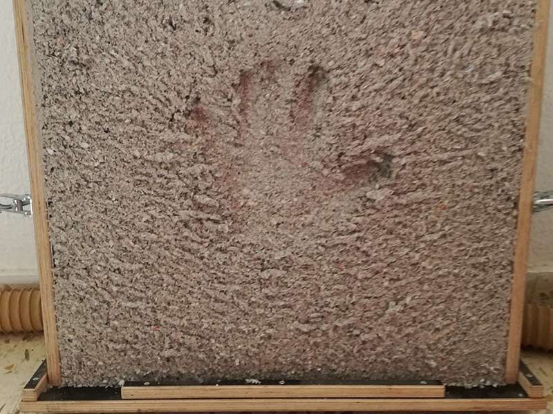 Una huella de mano impresa en una superficie cuadrada texturizada de color gris claro, enmarcada en madera.