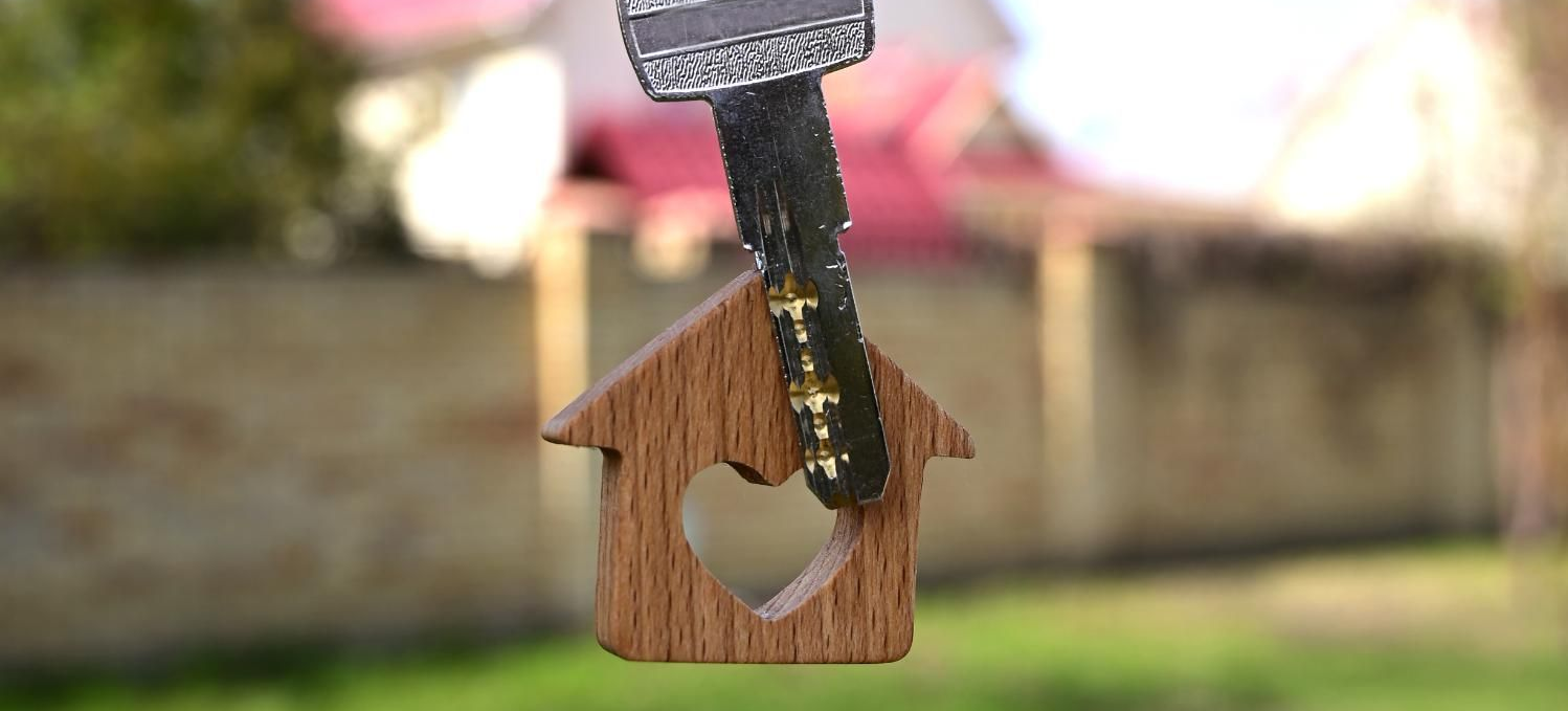 Llave con charm en forma de casa, al aire libre con fondo difuminado de una casa y vegetación.