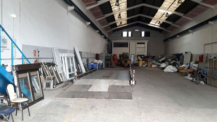 Interior de almacén con ventanas, materiales, rampa y artículos variados, en su mayoría blancos y azules.