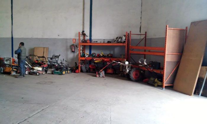 Hombre en un almacén rodeado de equipos, estanterías y herramientas. Paredes grises y suelo de hormigón.