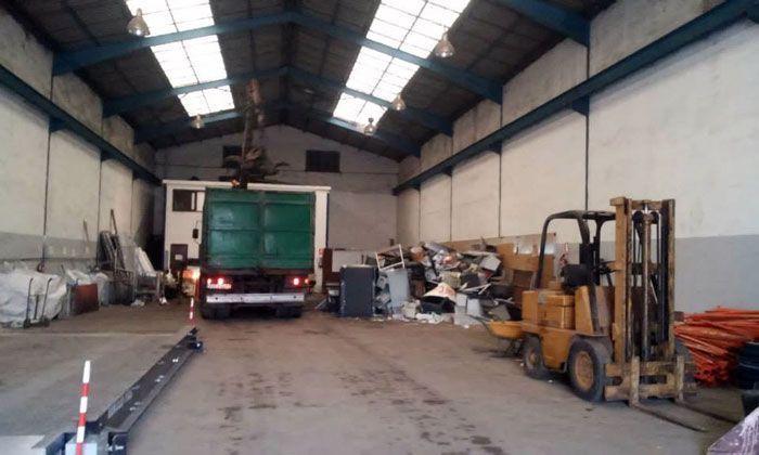 Dentro del almacén: camión en carga, carretilla elevadora, pila de artículos, tragaluces.