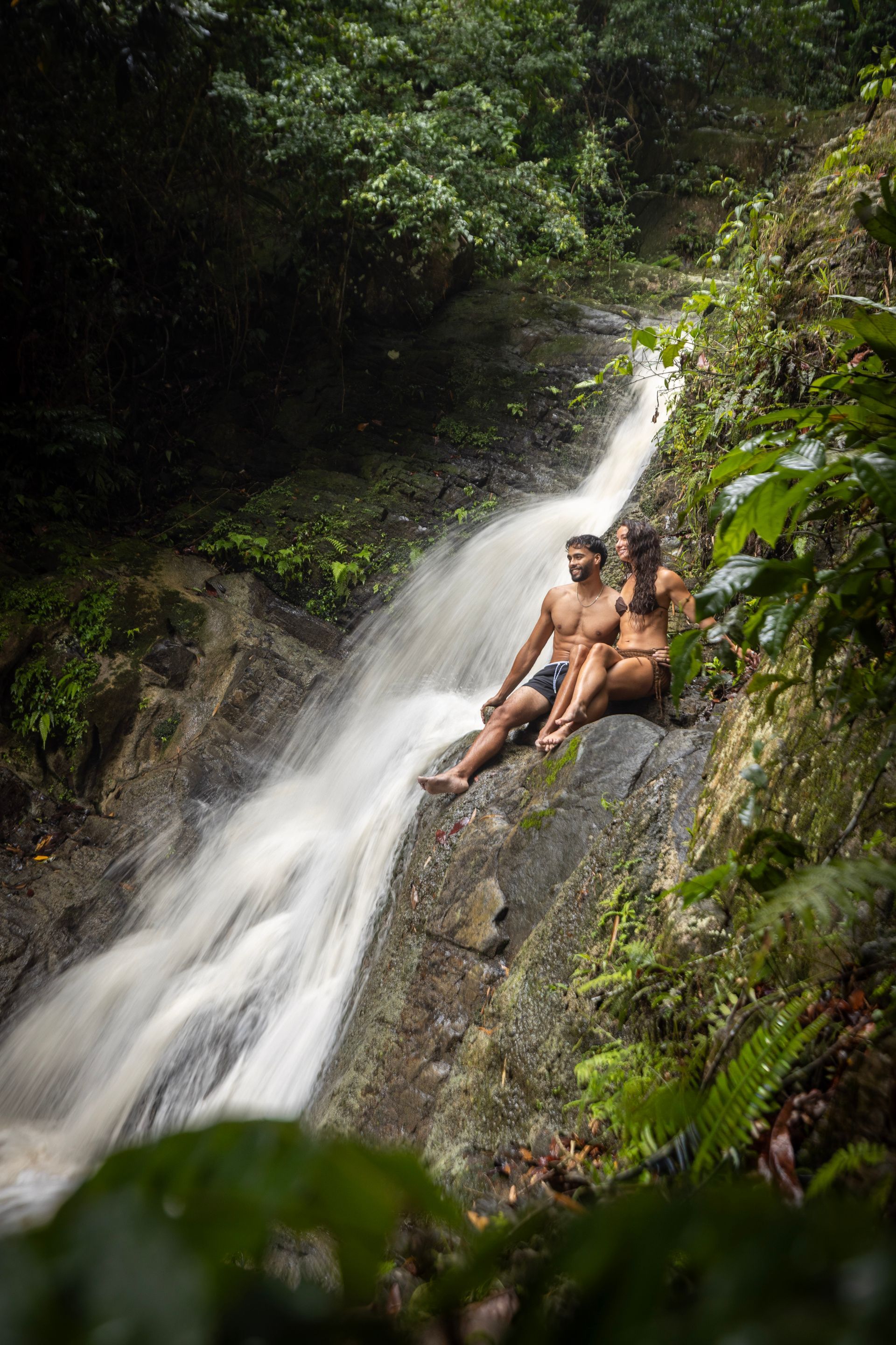 A couple sitting beside cascading waterfalls in the Jungle